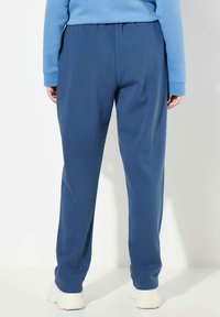 Niebieskie dresy o luźnym kroju, z elastycznym pasem i miękką strukturą, zestawione z jasnoniebieską bluzą i białymi sneakerami.