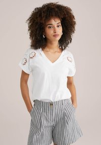Witte katoenen t-shirt met een V-hals en verfijnde oogjesdetails op de schouders, gecombineerd met gestreepte high-waisted shorts.