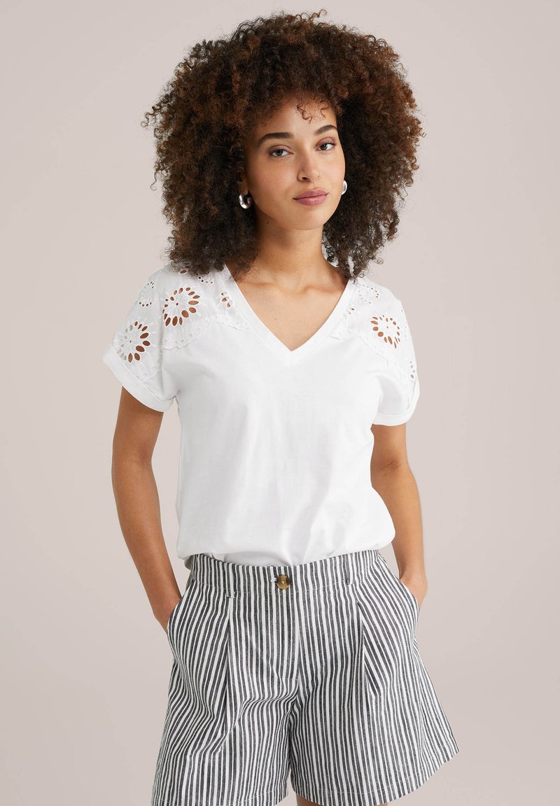 Witte katoenen t-shirt met een V-hals en verfijnde oogjesdetails op de schouders, gecombineerd met gestreepte high-waisted shorts.