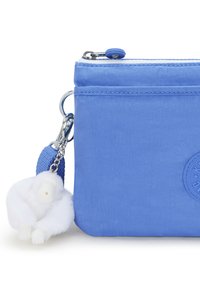 Blå nylonväska med en slät yta, med en rund logotyp och en fluffig vit gorilla nyckelring fäst vid ett blått band.