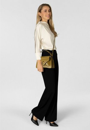 Pantalon noir à jambes larges associé à un haut à manches longues en satin crème. Un petit sac bandoulière vert olive avec un accent argenté est porté.