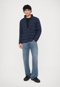 Jūras spēku puffer jaka ar rāvējslēdzēju priekšā, kam ir horizontāla quilted dizains. Apvienota ar gaiši ziliem taisnas kājas džinsiem un melnām kedām.