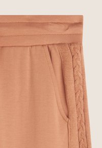 Pantalones deportivos de color melocotón con cintura elástica, bolsillo lateral y detalle de punto cableado texturizado a lo largo de la costura exterior. Material de algodón suave.