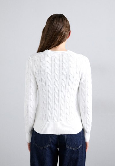 Weißer Strickpullover mit Rundhalsausschnitt, strukturiertem Muster und gerippten Bündchen und Saum. Kombiniert mit dunklen Jeans.