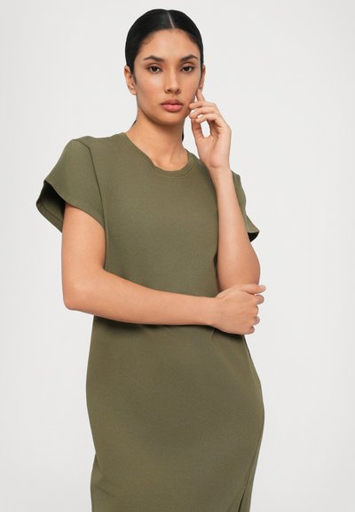 Olive green short-sleeve dress with a round neckline and slim fit. Smooth texture with a discreet side slit. Model poses with one hand on chin.