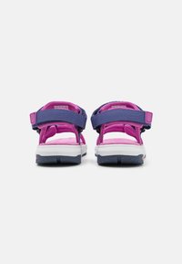 Pár fialových a růžových sandálů s otevřenou špičkou a nastavitelnými popruhy, viděný zezadu na jednoduchém bílém pozadí.