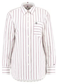 Chemise blanche à boutons avec des rayures verticales rouges, manches longues, une poche poitrine et un logo sur le côté gauche. Matière en coton, col classique.