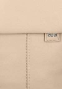 Zaino in pelle beige con parte superiore piegata, dettagli cuciti e una piccola etichetta del marchio con la scritta "zwei". Texture liscia e design minimalista.