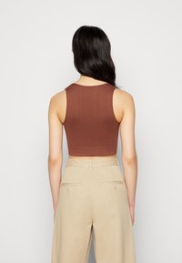 Top cropped castanho feito de tecido elástico, com decote redondo e design sem mangas, combinado com calças bege de cintura alta.