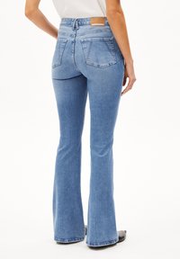 Uppvikta blå denimjeans med medelhögt midjeband, dekorativt sömnad och bakfickor; slät textur och läderetikett på midjebandet.