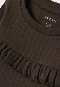 Brązowy, prążkowany top z okrągłym dekoltem i falbaną na dole. Materiał wydaje się miękki i ma teksturowane wykończenie.