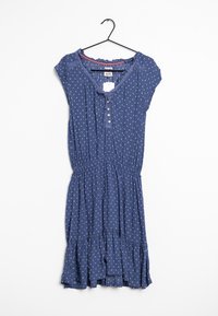 Sininen, lyhythihainen mekko, joka on valmistettu kevyestä kankaasta. Mekossa on valkoisia pilkkuja, nauhakiinnitys edessä, napit ja röyhelöhelma.