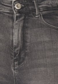 Tummanharmaat farkut, joissa on sileä pinta, metallinen nappisuljenta, etutasku ja hienovaraiset haalistumat.