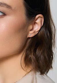 Złoty kolczyk w kształcie kwiatu z małymi białymi kamieniami. Kolczyk ma gładką teksturę i kompaktowy kształt, idealny do noszenia na co dzień.