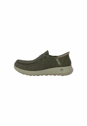 Zapato de tela texturizada verde con puntera redondeada, suela de perfil bajo y cordones elásticos. Presenta la marca en el costado y el talón.