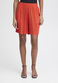 Rode, knielange shorts gemaakt van lichtgewicht materiaal met een elastische tailleband; gladde textuur en losse pasvorm. Vergezeld van zwarte sandalen.