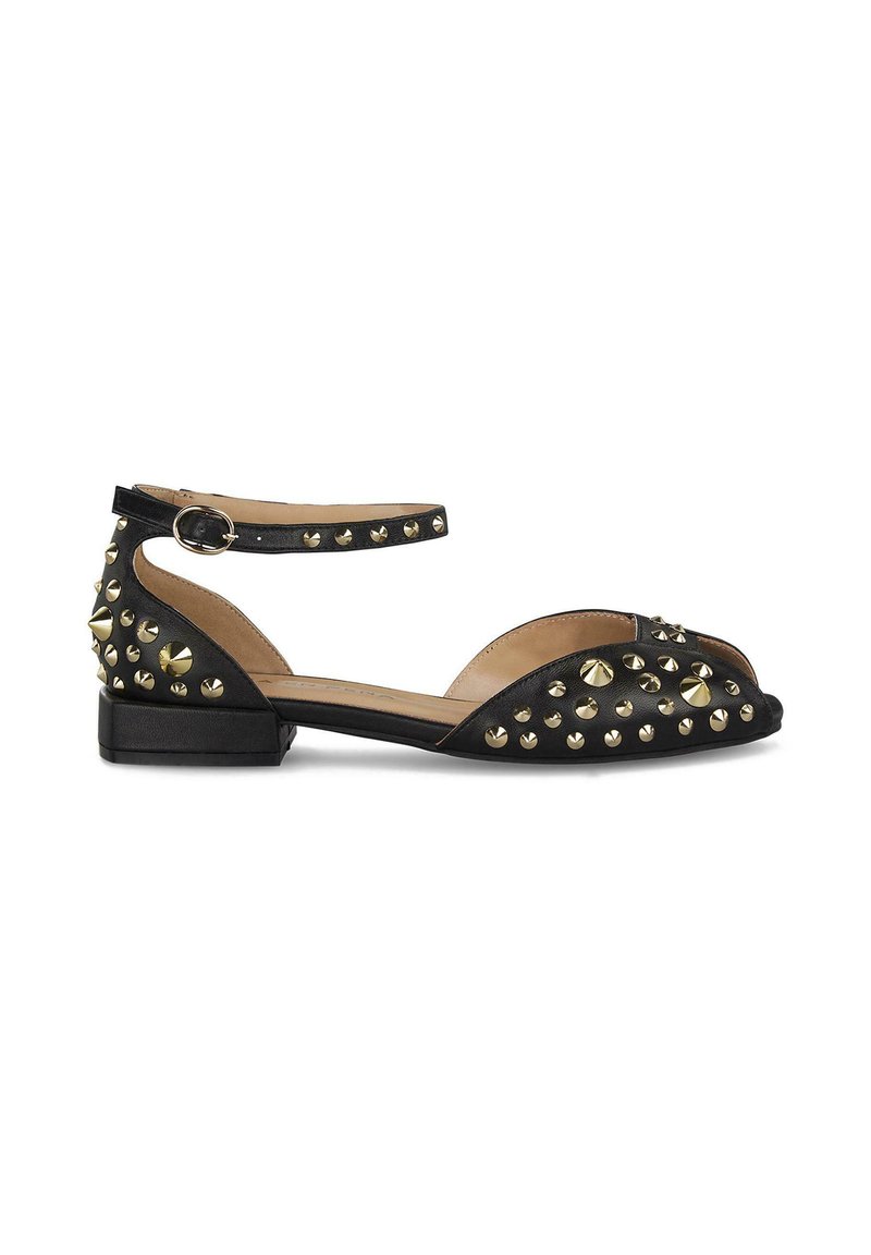 Zapatos planos negros con punta abierta, adornados con tachuelas doradas en la parte superior y una correa en el tobillo con una hebilla circular. Material de cuero texturizado.