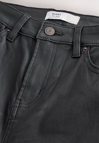 Crne uske traperice srednjeg struka s glatkom teksturom, s vidljivim prošivima, metalnim gumbom i oznakom na pojasu.