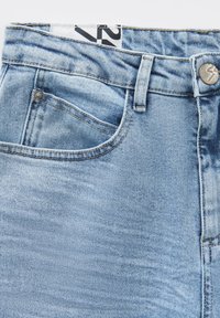 Light blue denim jeans with a five-pocket design, featuring a metal button closure, stitched detailing, and a brand label on the waistband.