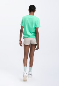 T-shirt in cotone verde menta, maniche corte, colletto rotondo, abbinato a pantaloni corti color sabbia. Sneakers bianche con calzini pastello, design minimalista.