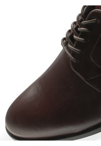 Botte en cuir brun foncé à lacets avec bout arrondi, coutures détaillées et semelle noire sur fond blanc.