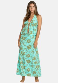 Turkisblå maxi-kjole med blomsterdesign og halterneck, med knyting og lagdelte volanger. Gyldent blomstermønster over hele kjolen.