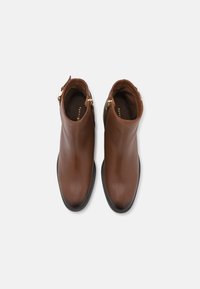 Botas de tobillo de cuero marrón con un acabado suave, puntera redondeada, cremalleras laterales y una suela negra baja. Sin patrones visibles ni detalles de hardware.