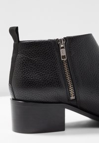 Schwarze Leder-Stiefelette mit strukturiertem Obermaterial, seitlichem Reißverschluss und Blockabsatz. Verfügt über ein elastisches Panel für optimalen Sitz und Langlebigkeit.