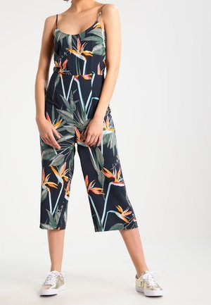 Kombinezon w kwiatowy wzór na granatowym tle, z regulowanymi ramiączkami, szerokimi, skróconymi nogawkami oraz jasnymi motywami rajskich ptaków.