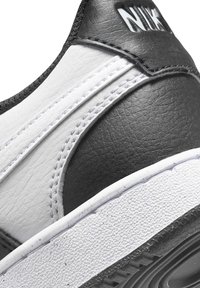 Sneaker Nike in bianco e nero con tomaia in pelle texturizzata, cuciture a contrasto e suola in gomma a motivo. Presenta un dettaglio del logo in evidenza.