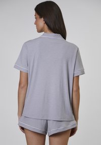Grå kortärmad pyjamasuppsättning med kragad topp och matchande shorts. Har vit piping på ärmar och shorts. Mjuk, texturerad tyg.