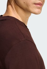 Hnedé bavlnené tričko s okrúhlym výstrihom, viditeľným prešitím na ramene a rukáve a hladkou textúrou.