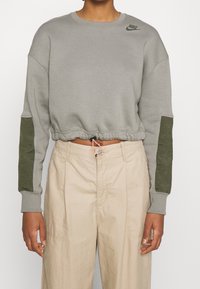 Grå kortärmad sweatshirt med gröna akcentfickor på ärmarna, ribbad halsringning och muddar, med en liten mörkgrå logotyp på bröstet.