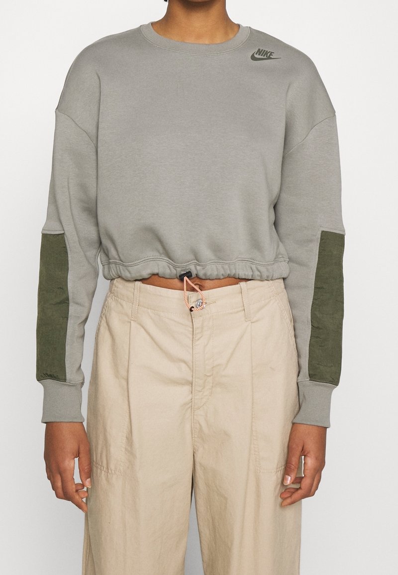 Grå kortärmad sweatshirt med gröna akcentfickor på ärmarna, ribbad halsringning och muddar, med en liten mörkgrå logotyp på bröstet.