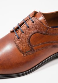 Braunes Leder-Dress-Schuh mit strukturierten Akzenten, schlankem Design, kontrastierenden blauen Schnürsenkeln und glatter Oberfläche. Verfügt über eine runde Spitze und gestickte Details.