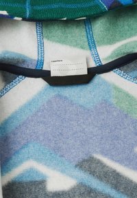 Polarowy pulower w zielone, niebieskie i szare geometryczne wzory. Posiada czarną pętelkę do zawieszenia oraz metkę informacyjną wewnątrz. Miękka faktura.