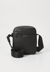 Black leather crossbody bag with a textured finish, featuring a front zipper pocket and an adjustable fabric strap. Brand logo visible.