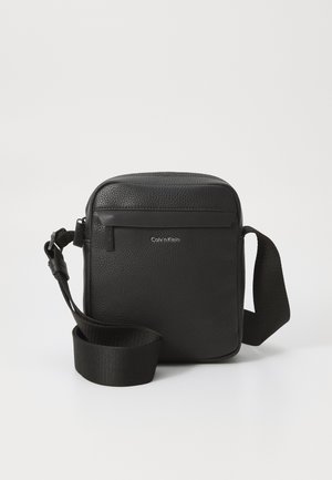 Borsa a tracolla in pelle nera con finitura texturizzata, dotata di una tasca frontale con zip e di una tracolla in tessuto regolabile. Logo del marchio visibile.