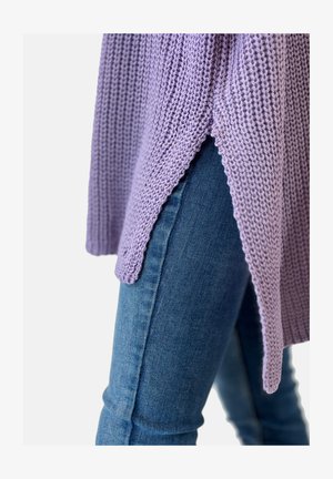 Close-up of side slit lavender knitted sweater worn over blue denim jeans on a person.