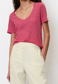 Krótki rękaw, t-shirt z dekoltem w serek w miękkim, różowym materiale. W zestawieniu z jasnobeżowymi spodniami na elastycznej talii. Prosty, casualowy design.