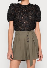Haut en dentelle florale noire avec des manches courtes bouffantes, associé à un short taille haute vert olive avec un lien à l'avant et un détail de bouton.