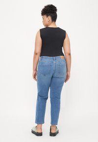 Crna majica bez rukava, svijetloplave hlače s visokim strukom i stražnjim džepovima, te zelene cipele. Glatka tkanina s klasičnom denim teksturom.