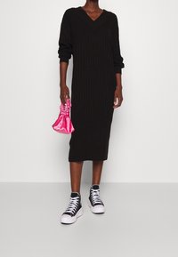 Abito midi a coste nere con scollo a V e maniche lunghe, abbinato a sneaker alte in bianco e nero e una borsa di satin rosa.