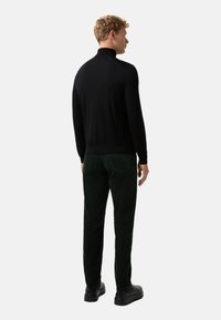 Schwarzer Rollkragenpullover mit langen Ärmeln, figurbetontes Design, getragen mit dunkelgrünen Cordhosen und schwarzen Schuhen, von hinten betrachtet.