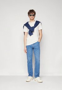 Balti marškinėliai, šviesiai mėlynos džinsai ir kasdieniai balti batai. Tamsiai mėlynas megztinis užmestas ant pečių, akiniai nuo saulės, tiesaus kirpimo kelnės.