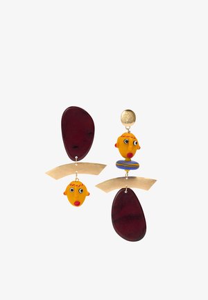 Asymetryczne kolczyki z abstrakcyjnymi żółtymi twarzami, czerwonymi ustami, złotymi zakrzywionymi prętami i ciemnofioletowymi owalnymi kształtami na białym tle.