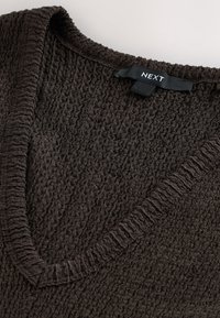 Gros plan sur un tissu tricoté texturé marron foncé avec un col en V côtelé et une étiquette noire de vêtement indiquant NEXT.