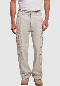 Béžové cargo kalhoty s elastickým pasem, několika bočními kapsami, rovný střih a nastavitelné manžety na kotnících, spárované s hnědou obuví.