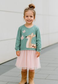 Hellgrüner Sweatshirt mit Bestickung von einem Reh und einem Schmetterling, kombiniert mit einem rosa Tüllrock und beigen Ankle Boots.