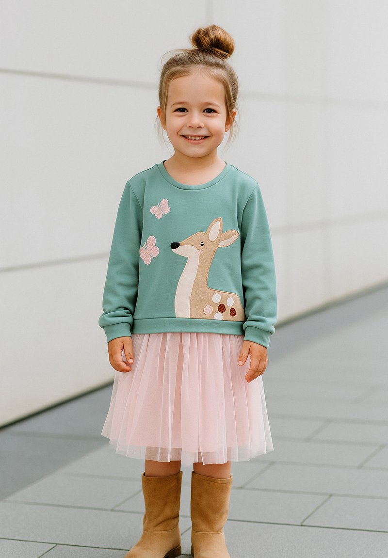 Hellgrüner Sweatshirt mit Bestickung von einem Reh und einem Schmetterling, kombiniert mit einem rosa Tüllrock und beigen Ankle Boots.